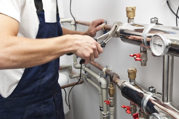 The man is installing the heater system in the house and checking pipes by the wrench